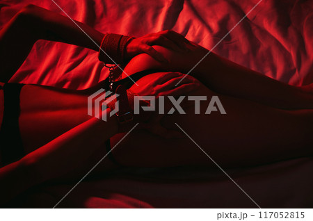 submissive woman girl with a sexy body and ass in panties with handcuffed hands lying on bed in bedroom. BDSM sex with submission and domination with red neon light 117052815