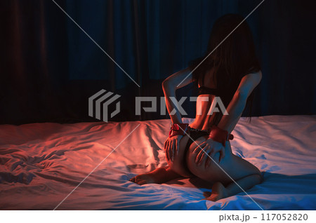 submissive sexy woman with hands in BDSM handcuffs with beautiful ass in underwear is sitting on bed. Slave girl with a slender naked body for hard sex with submission and domination 117052820