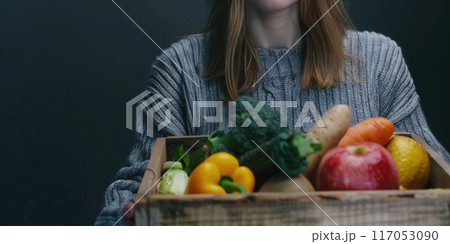 A woman is holding a wooden crate full of fruits and vegetables 117053090