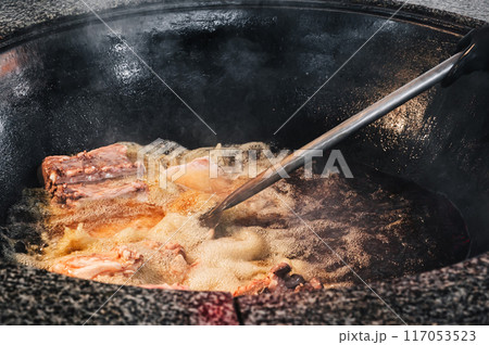chef cooks lamb meat in a boiling cauldron for traditional oriental Uzbek pilaf in kitchen of a restaurant in Uzbekistan 117053523