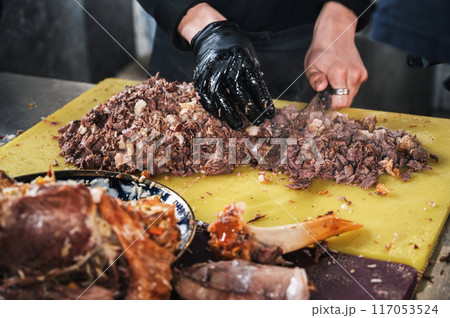 male chef cut boiled lamb meat with a knife to cook asian Uzbek pilaf in restaurant in Central Asian Pilaf Center in Tashkent in Uzbekistan 117053524