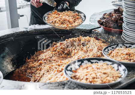 hands of a male chef cooking traditional oriental Arabic Uzbek rice pilaf with meat lamb in cauldron. Central Asian Pilaf Center Besh Qozon in Uzbekistan in Tashkent 117053525