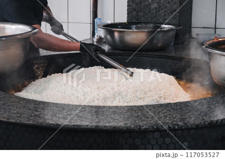 man cook cooking traditional oriental Asian Uzbek rice pilaf in a large cauldron in restaurant in Uzbekistan 117053527