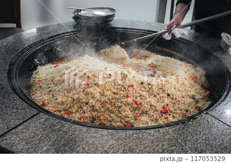male chef prepares traditional Asian Uzbek rice pilaf in a large cauldron in kitchen of a restaurant in Tashkent in Uzbekistan 117053529