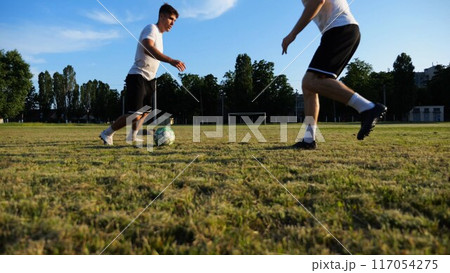 Two sportsmen playing in soccer in stadium at sunset. Professional footballers performing tricks with ball at green field. Young men training at meadow. Concept of a freestyle football. Slow motion Two sportsmen playing in soccer in stadium at sunset. Professional footballers performing tricks with ball at green field. Young men training at meadow. Concept of a freestyle football. Slow motion 117054275