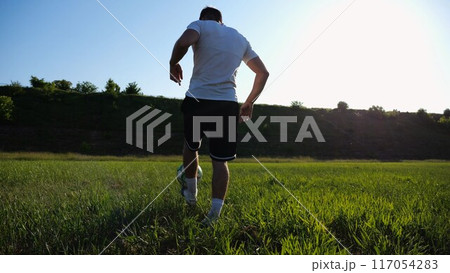 Sportsman juggling soccer ball on stadium at sunny day. Young man kicking ball at green field. Professional footballer practicing tricks at meadow with sunlight at background. Freestyle football. Sportsman juggling soccer ball on stadium at sunny day. Young man kicking ball at green field. Professional footballer practicing tricks at meadow with sunlight at background. Freestyle football. 117054283
