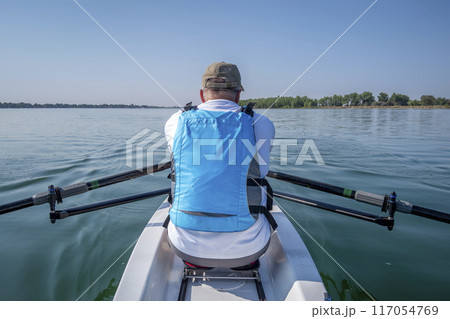 senior male in a rowing shell on calm lake, POV from a boat bow senior male in a rowing shell on calm lake, POV from a boat bow 117054769