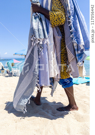 Beach Vendor Draped in Colorful Towels on Sandy Shore Beach Vendor Draped in Colorful Towels on Sandy Shore 117056442