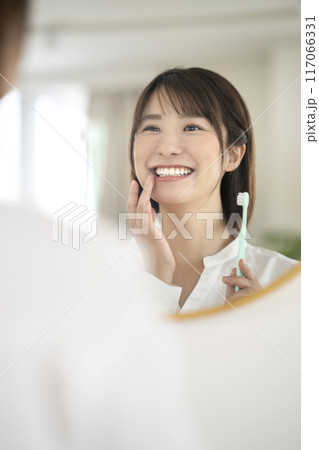 鏡を見ながら歯磨きをするアラサーの女性 鏡を見ながら歯磨きをするアラサーの女性 117066331