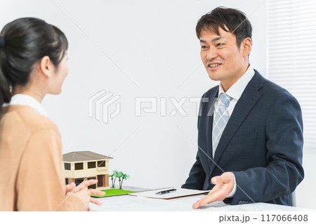 不動産会社のカウンターで物件・部屋探しの相談を受ける男性ビジネスマンと顧客の女性 117066408