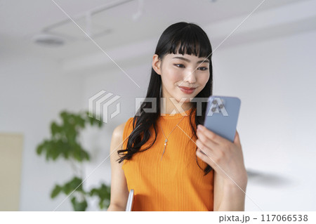 オフィスでスマートフォンの画面を見る若いビジネスウーマン オフィスでスマートフォンの画面を見る若いビジネスウーマン 117066538