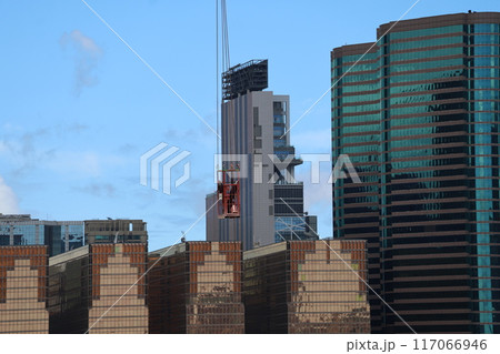 青空と高層ビルの大都会の街並みの中に吊り下げられたクレーンの滑車かごが見える風景 117066946