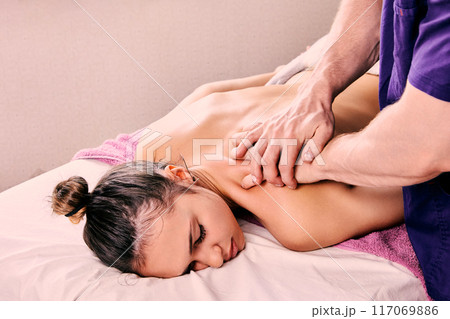 Beauty spa, male masseur gives back massage to young woman about 20 years old lying on massage table. 117069886