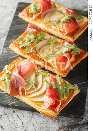 Appetizer pear jamon puff pastry pies for buffet and parties close-up on marble board. Vertical 117072619