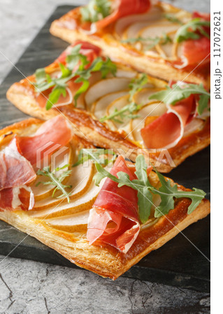 Puff pastry sandwich with pear, ham and arugula close-up on marble board. Vertical 117072621