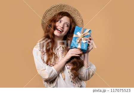 Happy woman gift box on beige background. Lady smiling,interested what's inside 117075523