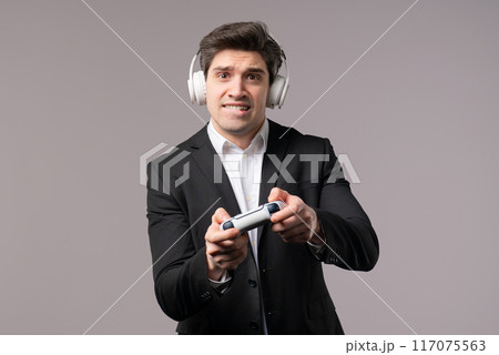 Handsome young businessman playing video exciting game on Tv with joystick isolated on grey studio background. Using modern technology. Handsome young businessman playing video exciting game on Tv with joystick isolated on grey studio background. Using modern technology. 117075563