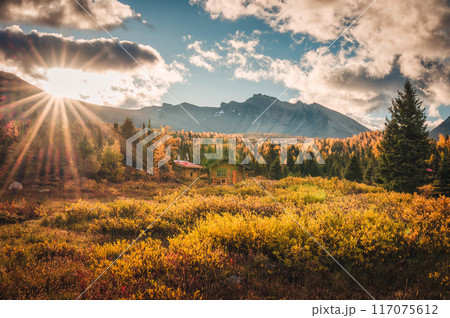 Sunrise shining over wooden huts with rocky mountains in autumn forest at Assiniboine provincial park, Canada Sunrise shining over wooden huts with rocky mountains in autumn forest at Assiniboine provincial park, Canada 117075612