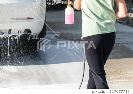 A young girl enthusiastically assists in washing the family's electric car in their suburban driveway. A young girl enthusiastically assists in washing the family's electric car in their suburban driveway. 117077715