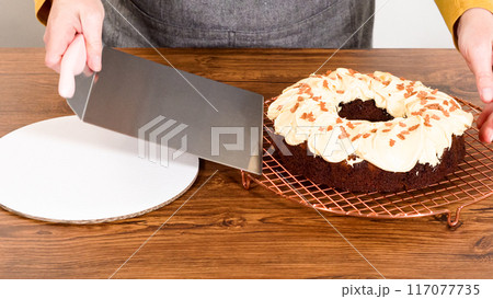 Carefully placing the gingerbread bundt cake, adorned with salted caramel frosting and gingerbread sprinkles, into a white paper bundt cake box with a clear window for gifting. Carefully placing the gingerbread bundt cake, adorned with salted caramel frosting and gingerbread sprinkles, into a white paper bundt cake box with a clear window for gifting. 117077735