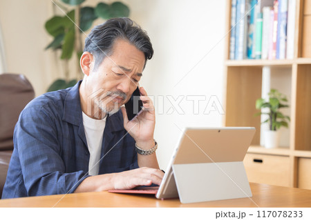 スマホで電話をしながらパソコンを操作するシニア男性 117078233