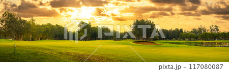 Golf course at sunset with dramatic sky and sand trap. Picturesque panoramic view of putting green with bunker 117080087