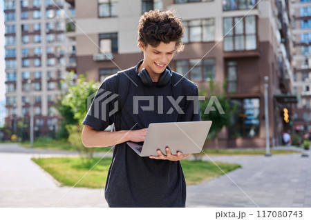 Young male college student with backpack headphones using laptop, outdoor 117080743