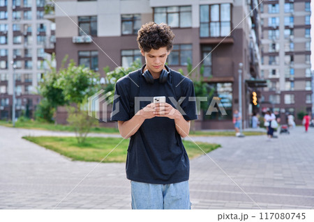 Walking young guy using smartphone, modern city street background 117080745