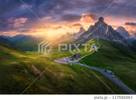 Aerial view of road in mountain pass, green meadows at sunset 117080863