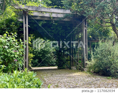 Wooden pergola gate in the garden with green leaves and trees. Wooden pergola gate in the garden with green leaves and trees. 117082034
