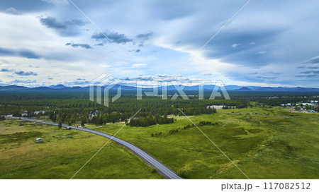 Aerial Fly Over Lush Green Field and Mountain Range with Winding Rural Road 117082512