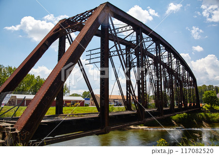 Rustic Truss Bridge over River with Industrial Backdrop Rustic Truss Bridge over River with Industrial Backdrop 117082520
