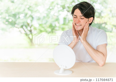 鏡を見ながら顎・頬を気にする若いアジア人男性（顎関節症・歯ぎしり・乾燥肌・スキンケア） 117084871