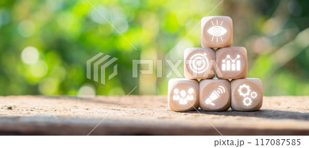 Wooden blocks with icons symbolizing vision, goals, strategy, and success, stacked in a pyramid against a natural background. 117087585