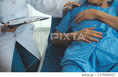 Hospitalized man lying in bed while doctor checking his pulse. Female physician examining male patient in hospital room. 117088017