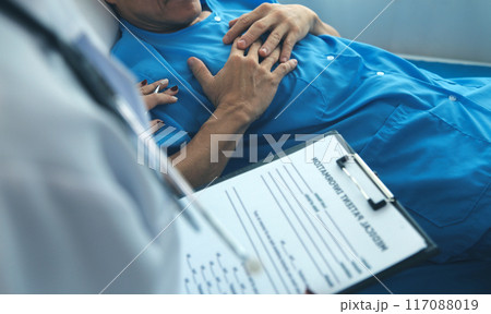 Hospitalized man lying in bed while doctor checking his pulse. Female physician examining male patient in hospital room. 117088019