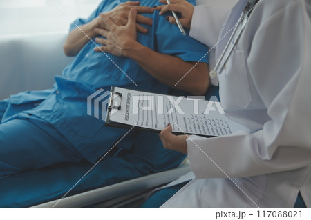 Hospitalized man lying in bed while doctor checking his pulse. Female physician examining male patient in hospital room. 117088021