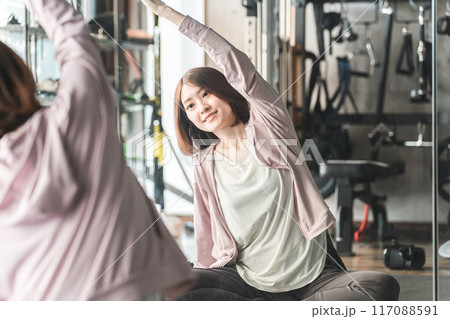 ジムのストレッチエリアでストレッチ・準備体操・柔軟体操をする若いアジア人女性 117088591