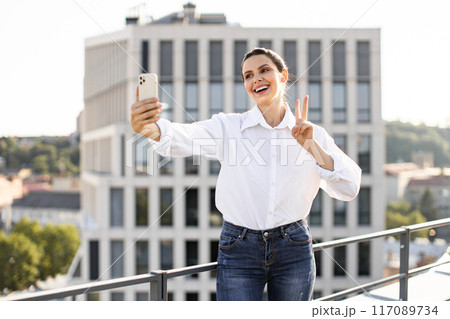 Woman taking selfie on rooftop making peace sign 117089734