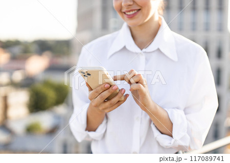 Young woman smiling while using her smartphone outdoors 117089741