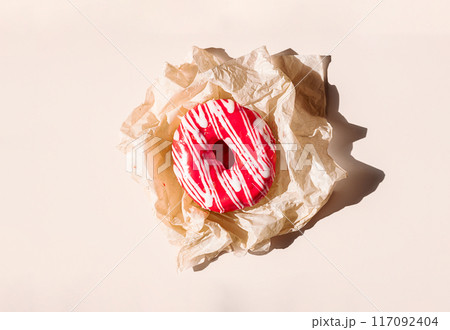 Pink glazed doughnut with white drizzle on crumpled parchment paper. 117092404