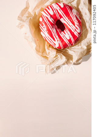 Pink glazed doughnut with white drizzle on crumpled parchment paper. 117092405
