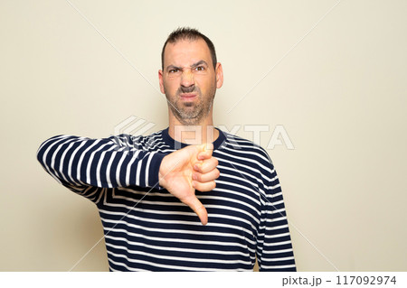 Bearded hispanic man about 40s wearing casual clothes looking unhappy and angry, showing rejection and negativity with thumbs down gesture. Bad expression. 117092974
