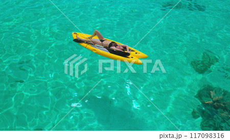 Woman relaxes on a paddle board in tropical waters, enjoying the sun and tranquility. The turquoise sea creates a peaceful backdrop for her carefree adventure. Perfect for summer vacation vibes Woman relaxes on a paddle board in tropical waters, enjoying the sun and tranquility. The turquoise sea creates a peaceful backdrop for her carefree adventure. Perfect for summer vacation vibes 117098316
