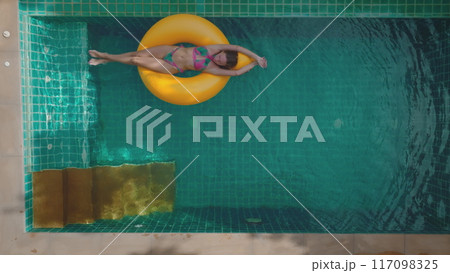 Young woman is enjoying her vacation, floating on yellow inflatable ring in swimming pool. Concept of summer vacation, relaxing in resort Young woman is enjoying her vacation, floating on yellow inflatable ring in swimming pool. Concept of summer vacation, relaxing in resort 117098325