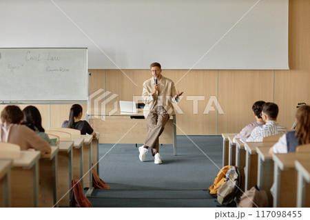 Wide angle shot of adult male teacher lecturing students on civil law speaking in hand held microphone in university classroom with whiteboard, copy space 117098455