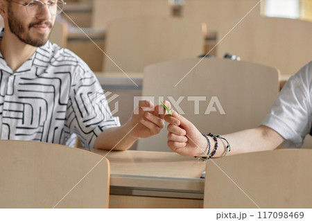 Cropped shot of male Middle Eastern student handing note to to his classmate while sitting at desk in university lecture hall, copy space 117098469