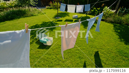 Clothes hang on a line in a sunlit backyard, casting shadows on the green lawn below. 117099116