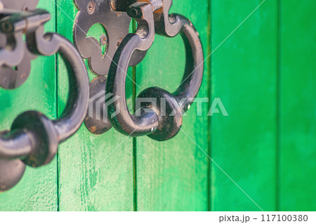 Iron forged handle bell on door with protruding part for easy hand grip to open or knock on door, thereby giving signal to open. Ancient devices, element of decoration created by forging metal 117100380