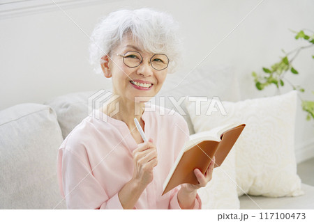 笑顔でスケジュール帳を持つシニア女性 カメラ目線 笑顔でスケジュール帳を持つシニア女性 カメラ目線 117100473